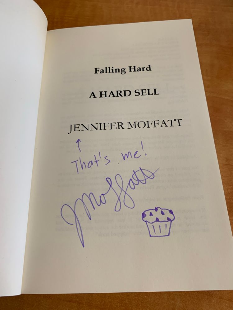 A photo of the title page of my book A Hard Sell with my autograph and a drawing of a chocolate chip muffin 