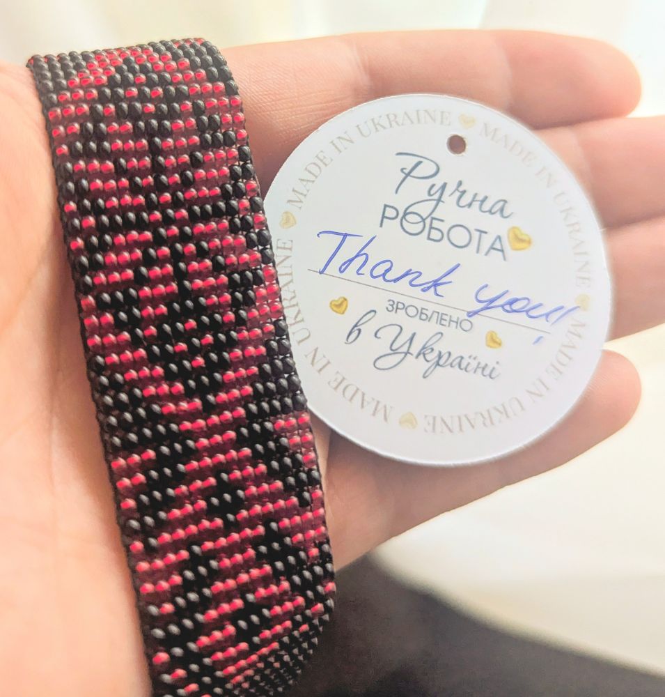 A beadwork bracelet with a red and black design and a tag that says 'made in Ukraine' and 'thank you' 