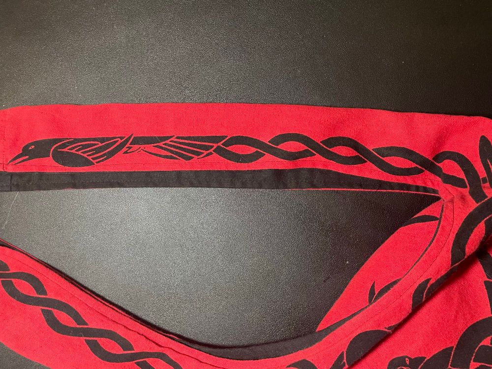 Detail of thick, crossbody strap. Fire engine red, cotton bag with black Celtic knot work design incorporating ravens. Exquisite design by Maxine Miller