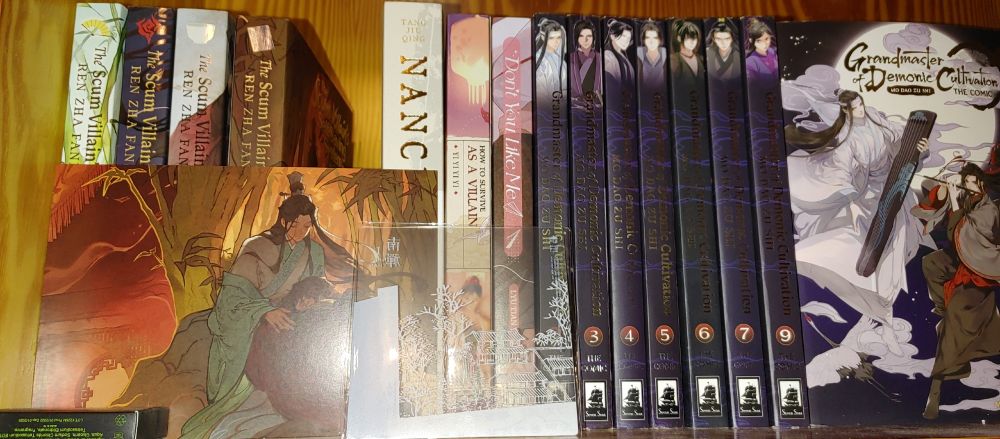 Wooden shelves with books: 
The Scum Villain's Self-Saving System 1-4, Nanchan 1, How To Survive As A Villain 1, Don't You Like Me 1, Grandmaster of Demonic Cultivation (Manhua) 1-7 & 9, with the 1st being on Display front cover-side (and behind it are Grandmaster of Demonic Cultivation [novel] 1-5 but not visible)