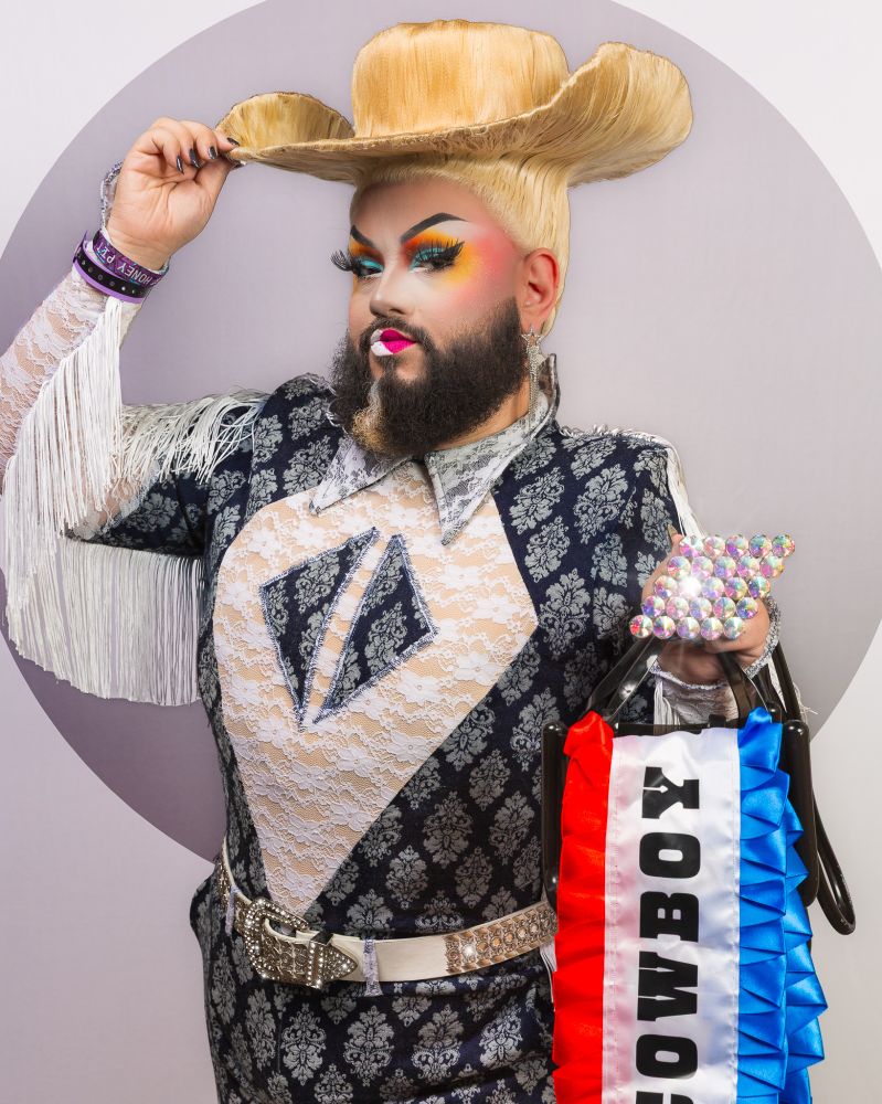 Just JP wears a cowboy hair hat wig, a denim and white lace and fringe bodysuit, a huge ring and a telfar with the cowboy carter sash cascading from it. JP looks at the camera with a confident expression
pic by spiff.bsky.social, bsky saw it first.