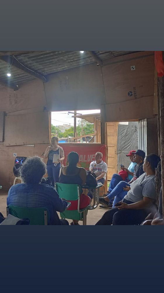Foto do barracão de reunião com pessoas sentadas me ouvindo falar, eu estou em pé segurando o microfone toda torta 