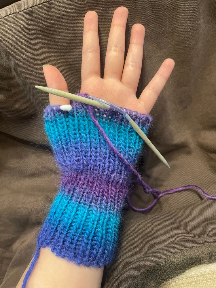 編みかけの手首カバーを手にはめた写真。青・水色・紫のグラデーション