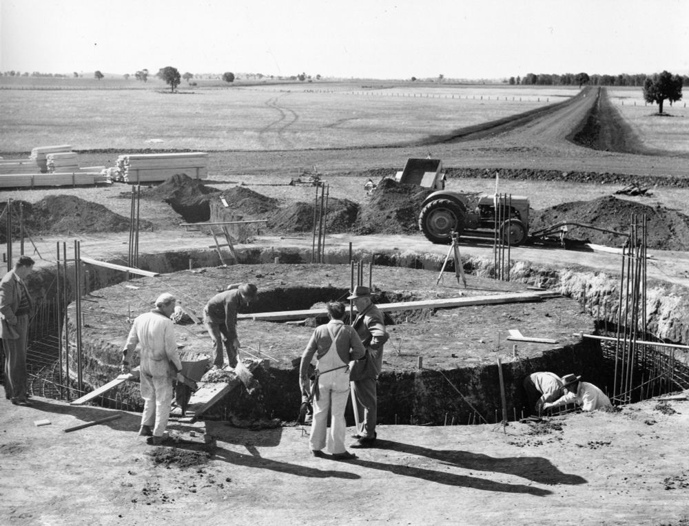 Old black and white photo of men working at building the base of the Parkes radio telescope, with a large ring that has been dug into the ground. 