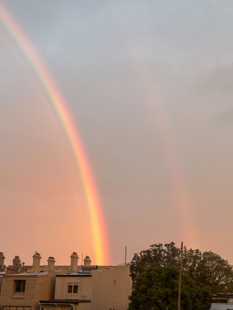 A bright and faint rainbow rising above buildings. 