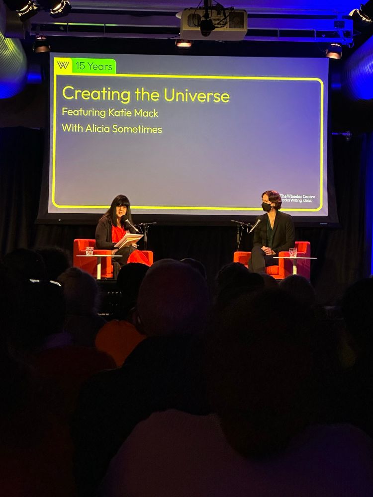 Alicia Sometimes and Dr Katie Mack on stage at an event. There is a screen behind them that reads “creating the universe feat. Katie Mack with Alicia Sometimes.