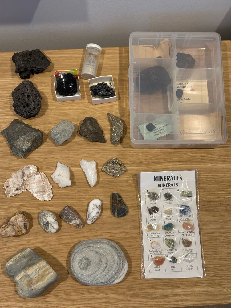 A collection of different old of shapes and sizes. All played out in a grid format in my side table. A small package of 12 minerals, all labelled nearby. Several meteorites inside a container. A small vile of volcanic ash also nearby. 