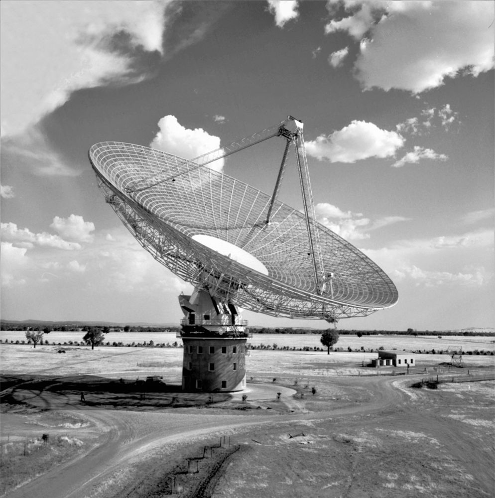 Old black and white image of the Parkes radio telescope in an open field. Taken during the early days of telescope operations.