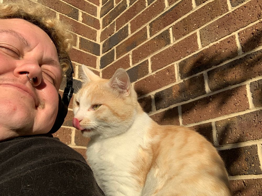 Frank and his human pose with their heads together, Frank is licking his own nose. 
