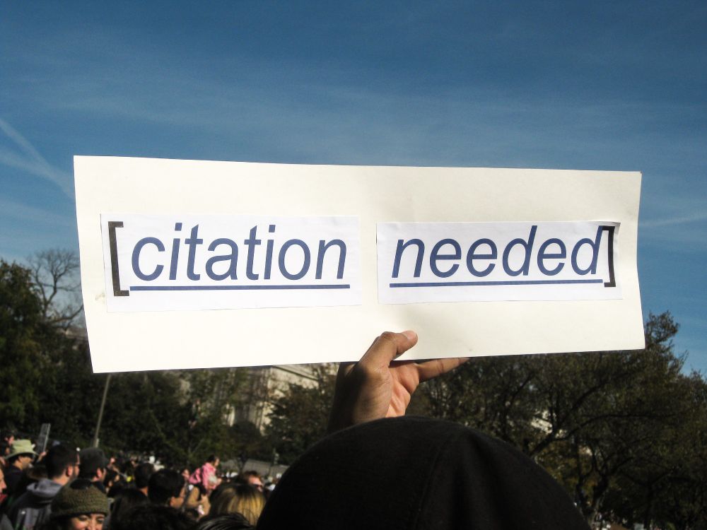 Hand holding a [citation needed] sign