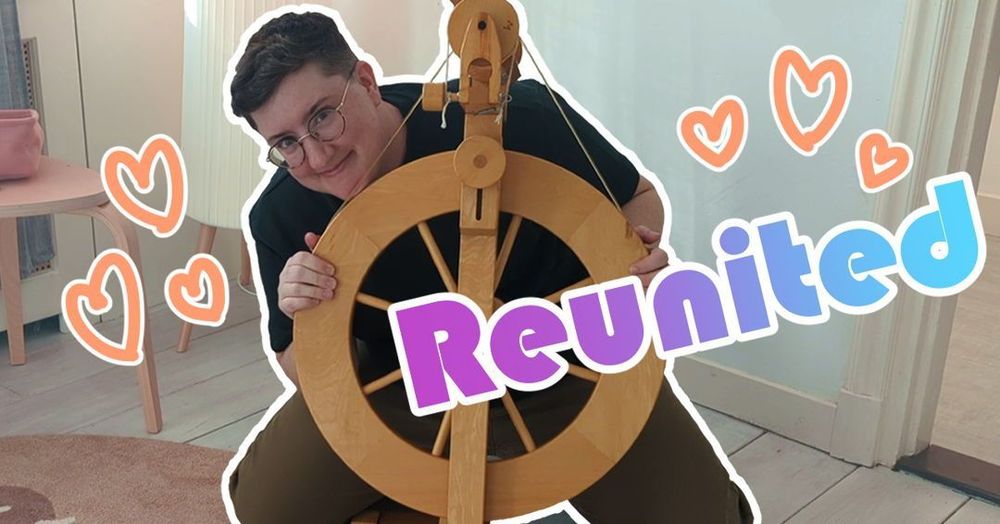 Youtube Thumbnail image. A castle style upright spinning wheel is in the center of the screen, and a white, dark haired person is crouched behind it, giving strong goblin energy with a delighted grin on their face. They're holding the wheel like some sort of prom photo. Superimposed over the image are orange hearts and the word "Reunited" in block print with a blue and purple gradient.