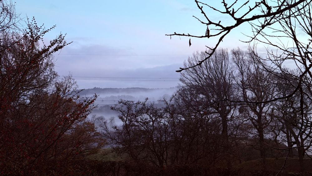 A landscape with fog hanging thick over a canal and hills