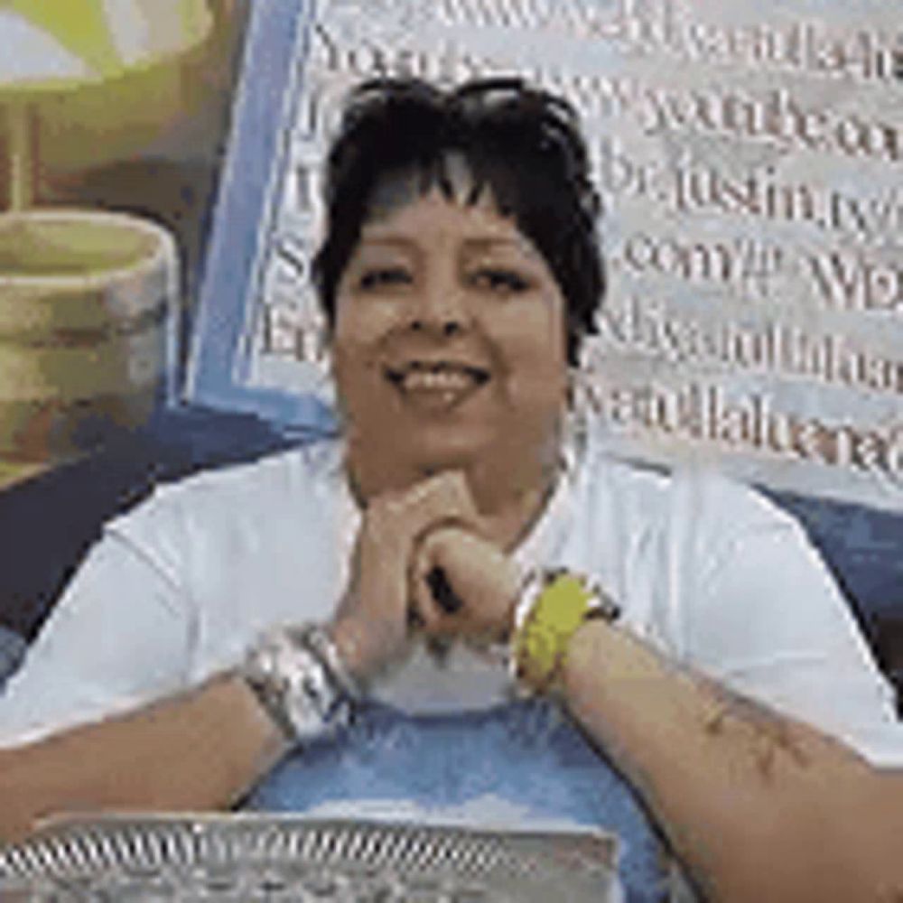 a woman is sitting at a table with her hands folded in front of a sign .