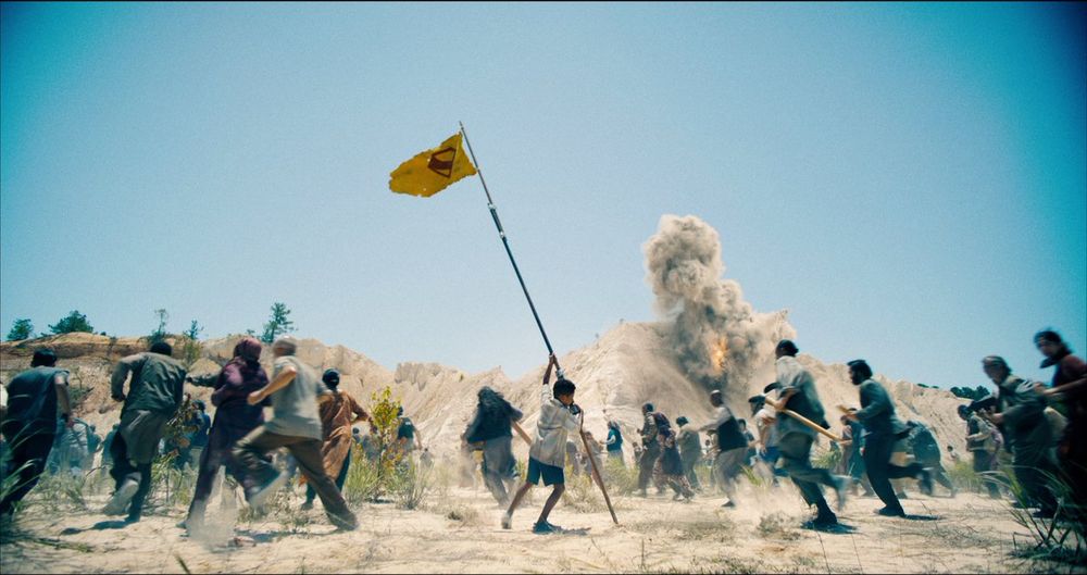 Jarhanpurian boy raising a Superman flag as Boravian soldiers bomb Jarhanpurian citizens during an invasion 