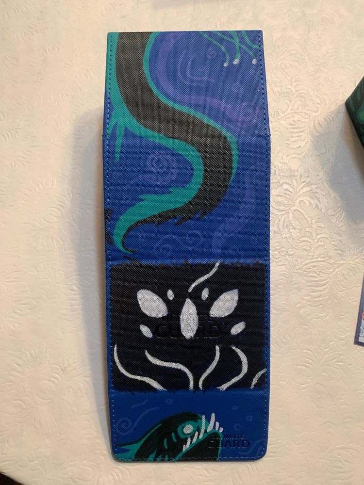 illustrations on a blue deck box featuring a closeup of a black creature with seven empty white eyes called krothuss, as well as a green and black serpent snaking around the deck box