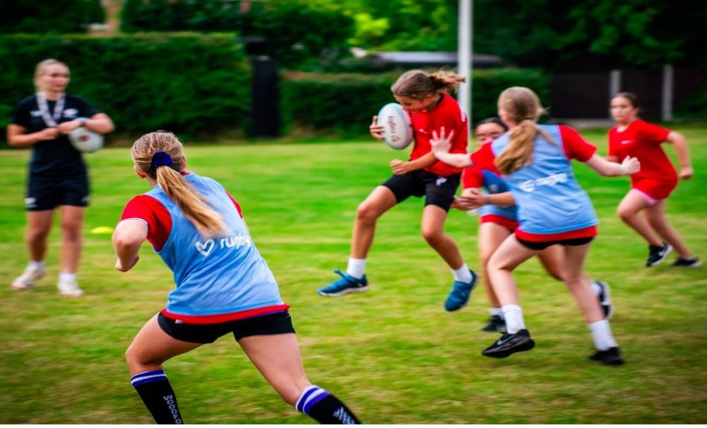 Photo of young women on the pitch playing rugby.