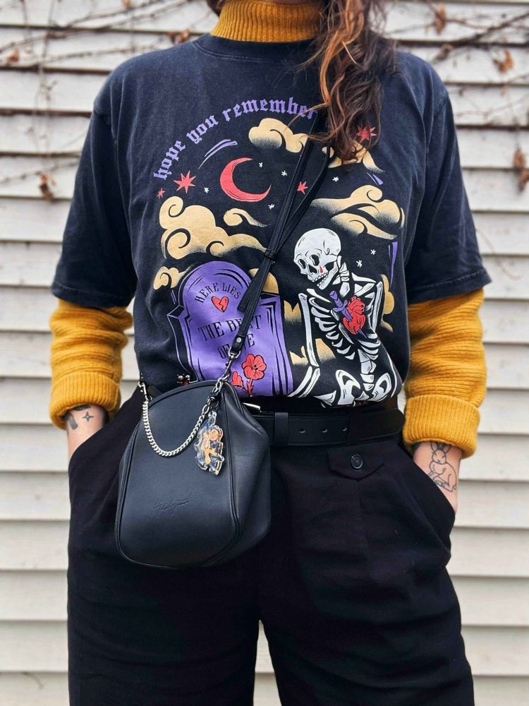 A person modeling Blooming Dream Co’s RPWP shirt. A skeleton sitting by a grave.