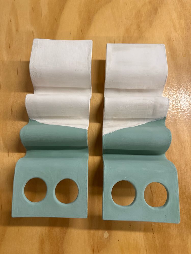 Two bisque fired ceramic taco stands with green glaze applied to one half and clear glaze applied to the other half. 