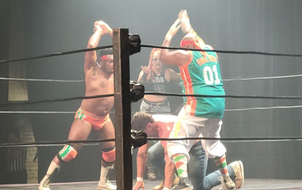 Two wrestlers attack another wrestler in the ring while he is trying to get back up.