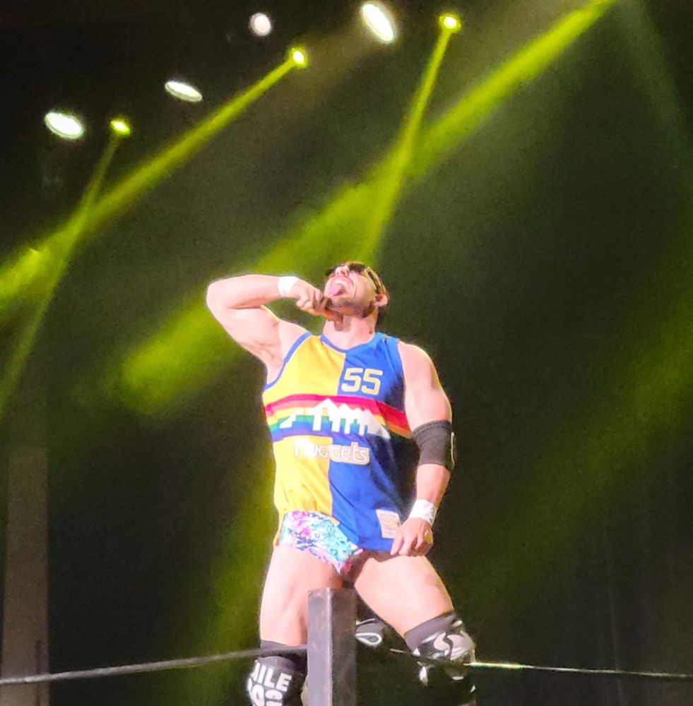 A wrestler poses on the turnbuckle wearing sunglasses and a Denver Nuggets jersey.
