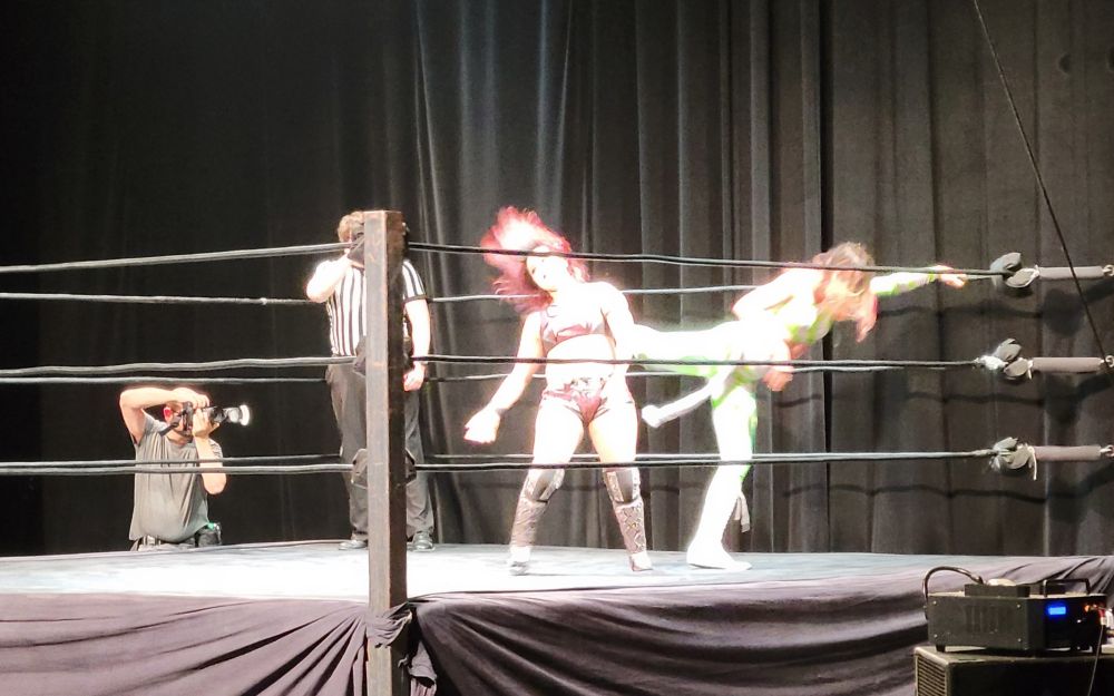 A wrestler kicks her opponent in the ring.