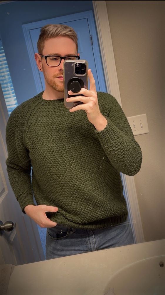 A bathroom mirror selfie of a guy wearing a green, textured hand knit sweater. 