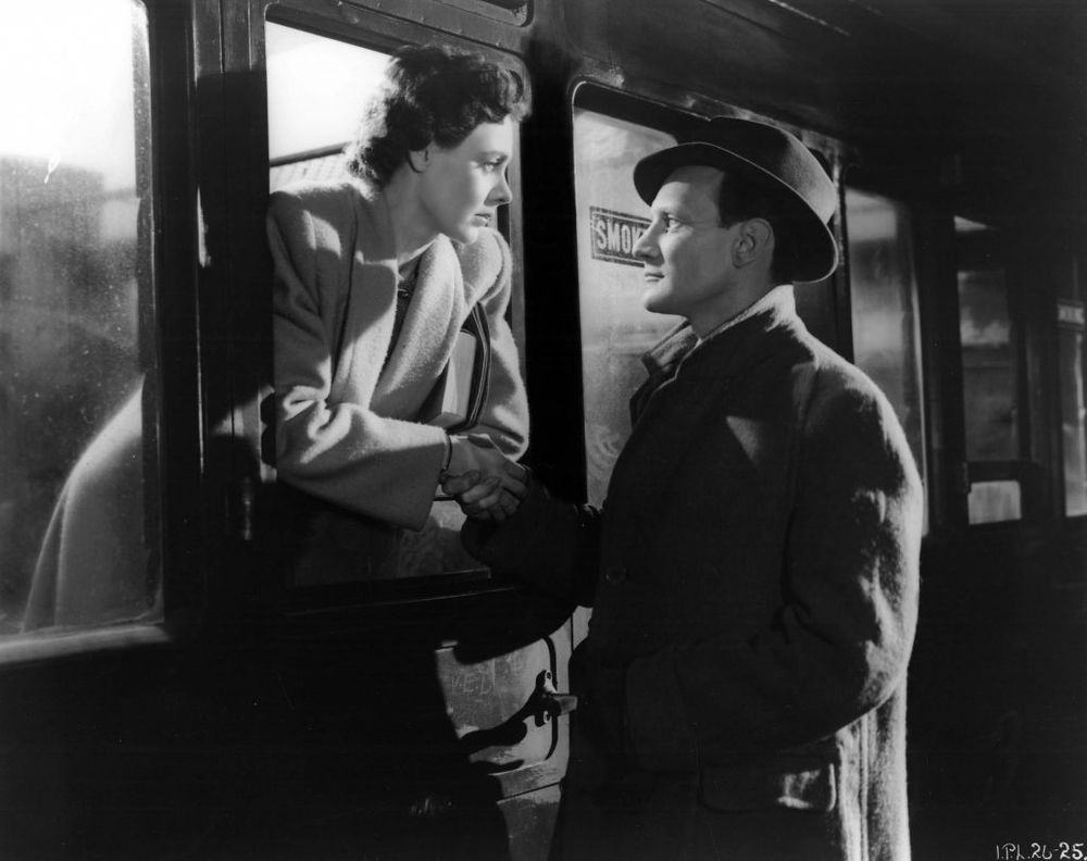 In a scene from Brief Encounter Laura leans through the open window of a train carriage while Alec stands on the station platform and they gaze at each other.