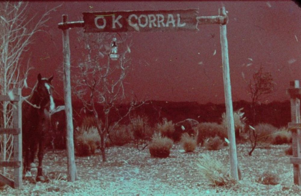 A scene with a dull red background. In the foreground is a mock old west set up with a big sign saying OK corral
