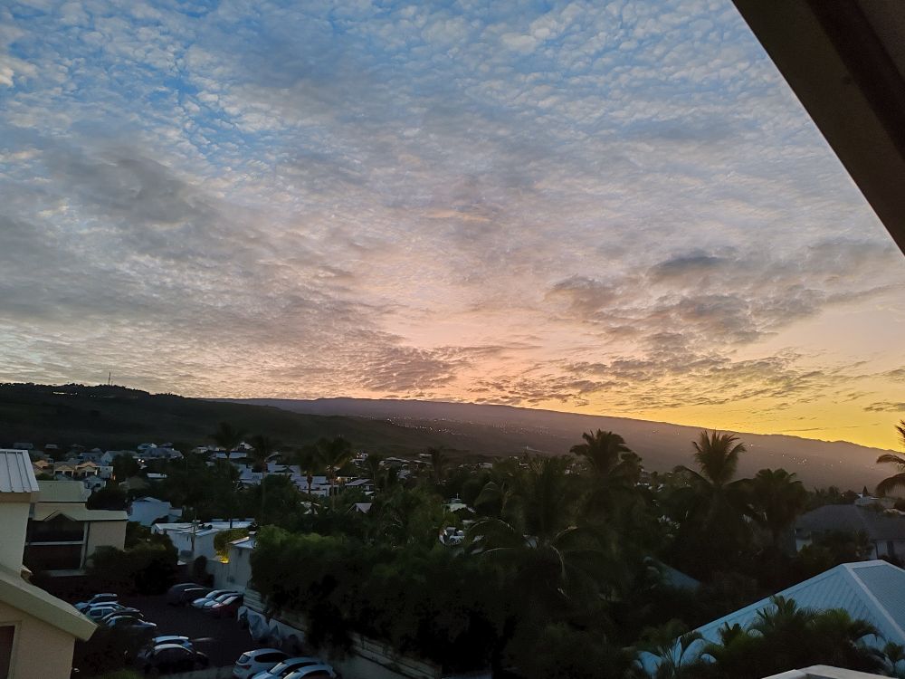 Derrière des toits et des arbres la montagne au lever du jour avec une légère lueur et quelques nuages 