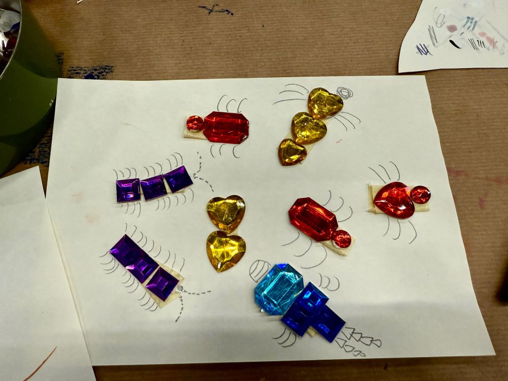 gem bugs on paper: blue, yellow and red gemstones of different sizes and shapes glued to paper and added pencil legs and antennas