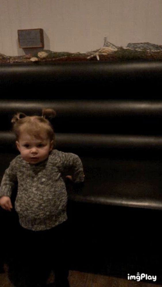 a little girl is standing in front of a black staircase and a sign that says ' imgplay ' on it