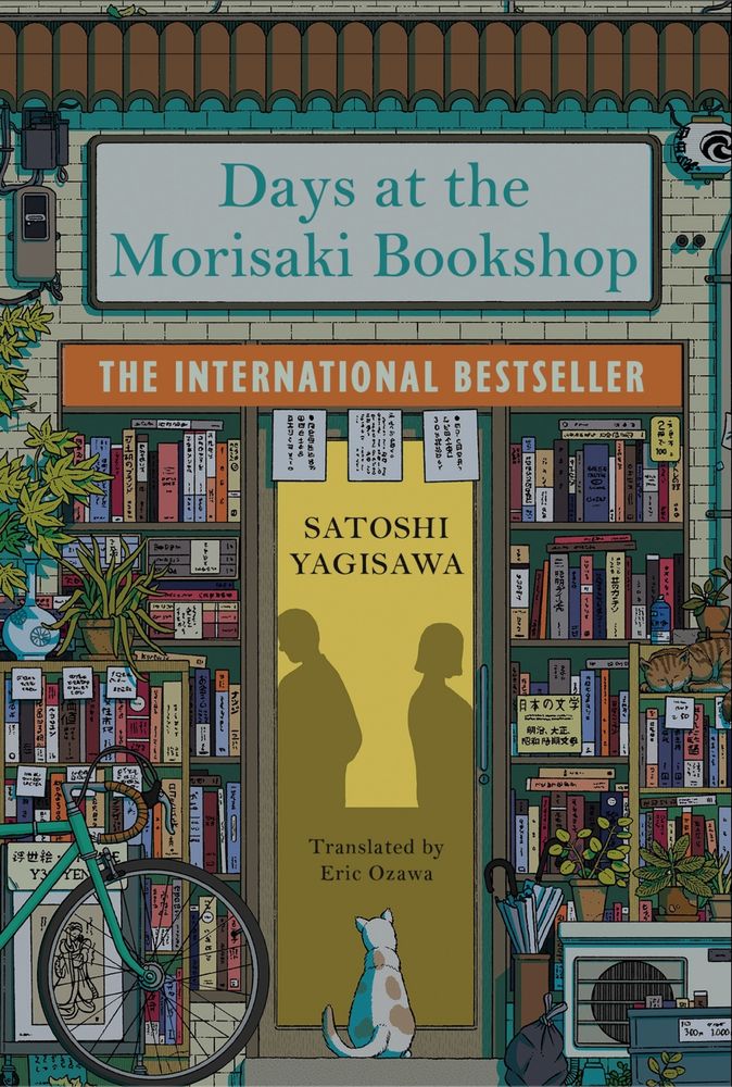 The cover of the ebook for the Japanese novel "Days at the Morisaki Bookshop" by Satoshi Yagisawa, translated to English by Eric Ozawa. It's an illustration of the outside of a bookshop, with shelves in front. A bike and a cat are positioned in front of the building. 