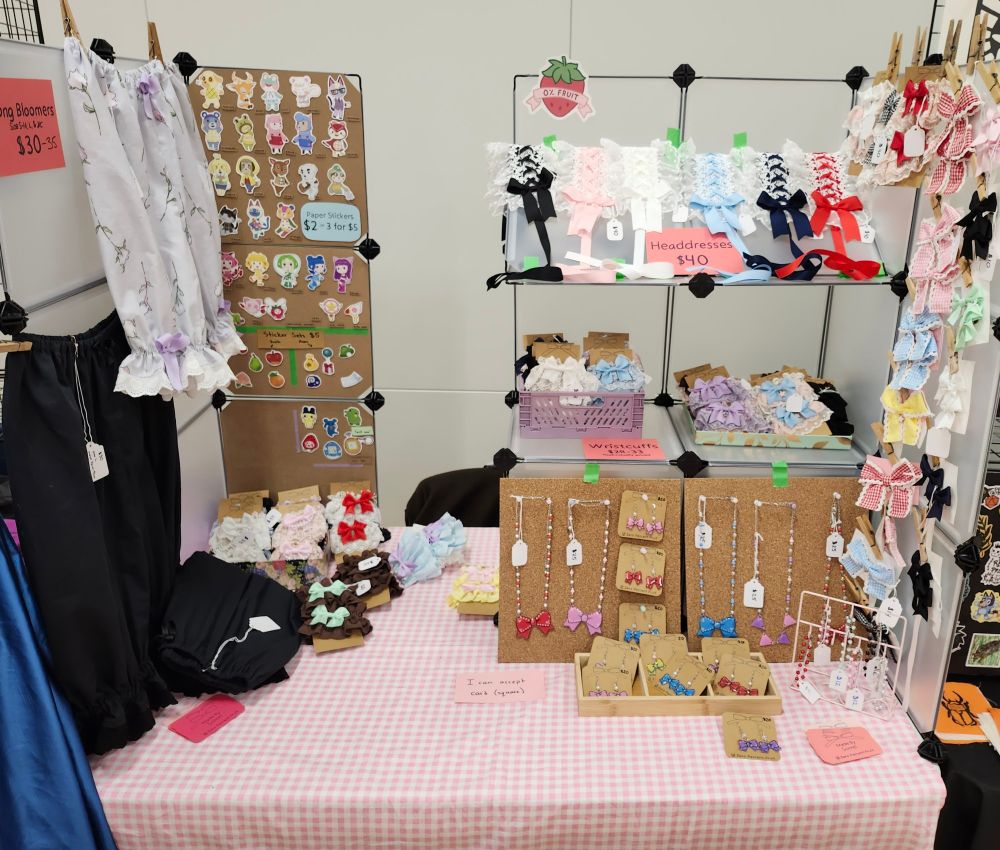 Picture of my table display for a convention. A setup made with grid cubes, a bit over 2 cubes have stickers, there's also a display of headdresses on one of the grid shelves. The left side has hanging pairs if bloomers