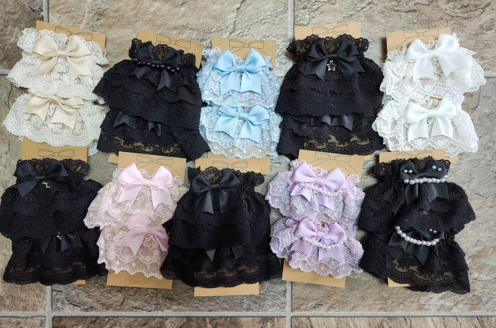 10 pairs of wristcuffs on brown cardstock backings. 5 of the pairs are black and are displayed with alternating light coloured pairs in a variety of colours.