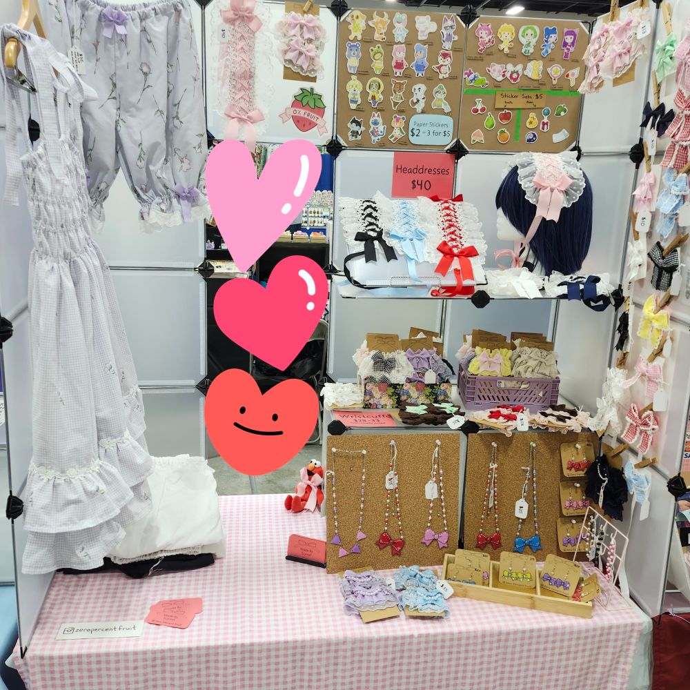 A table setup at a convention artist alley. The display is built on grid cubed and displays many egl fashion items and accessories (headdresses, wristcuffs, jewelry, bows, and bloomers)