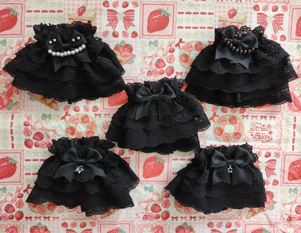 Five pairs of black mesh lace lolita wristcuffs, photographed on a piece of fabric with a repeating strawberry design.
Each pair has a slightly different decoration on the black bow at it centre, one is plain, two have charms, and two have fake pearl beads.