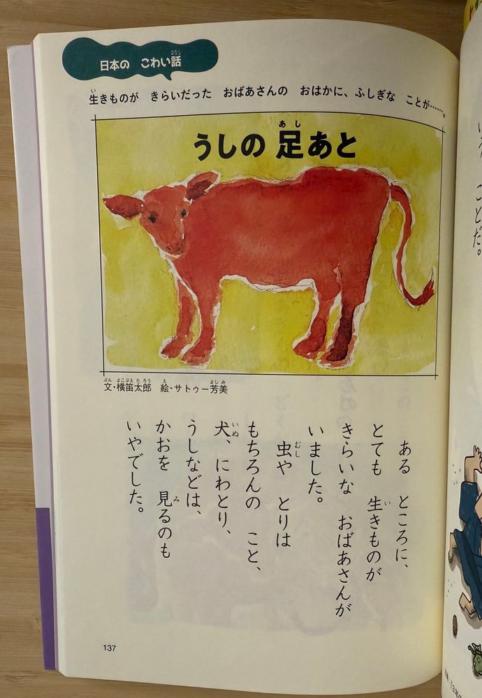 First page of a children’s spooky story in Japanese called The Cow’s Footprints. At the top of the page is a cute illustration of a red cow on a greenish-yellow background with the title above in Japanese. The illustration looks like it was painted in watercolors. And I cannot stress enough how cute this blankly staring cow is. This is important for the plot. 