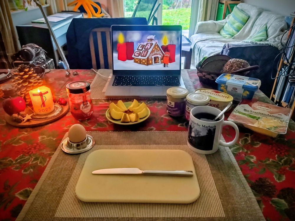 Ein gedeckter Frühstückstisch mit Apfel, Ei, Tee, Marmelade, Brotaufstrichen, Käse, Brot und Brötchen. Eine Kerze brennt, im Hintergrund zwei weitere Kerzen in der Sendung mit der Maus.