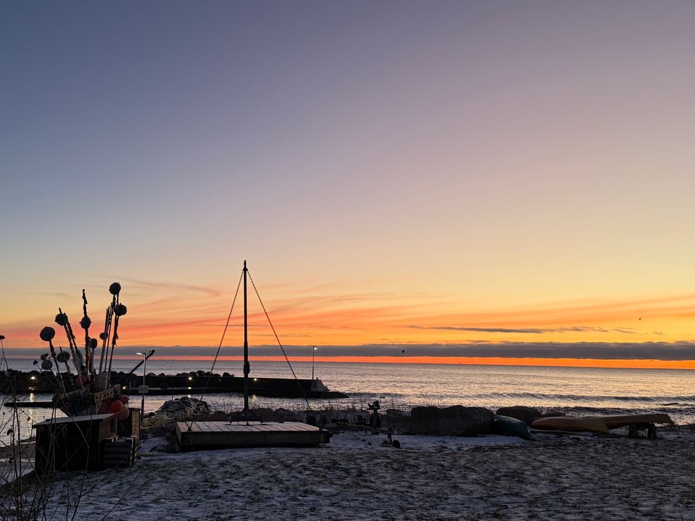 Sunrise over the Baltic Sea. Sand in the foreground, sea and sunrise in the background. To the left, a number of buoys stored on land.