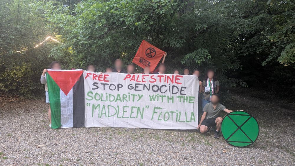 Plusieurs personnes tiennent une banderole où on peut lire "Free Palestine, Stop Genocide, Solidarity with the "Madleen" Flotilla", iels tiennent aussi des drapeaux de la Palestine et d'Extinction Rébellion