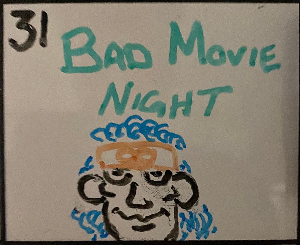 The 31st square of a whiteboard calendar stating “Bad Movie Night” followed by a dry erase marker depiction of Rem Lezar from straight to VHS masterpiece, ‘Creating Rem Lezar’