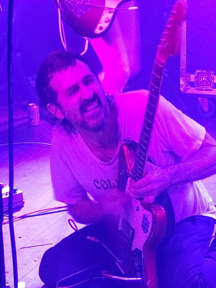 tropical fuck storm on stage at DC9 in Washington, DC, photo taken from side stage.  Gareth is on his knees playing guitar with an intense look on his face.