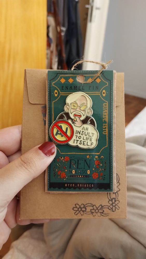 imagem de pin metálico com desenho do diretor japonês hayao miyazaki dizendo "ai is an insult to life itself"