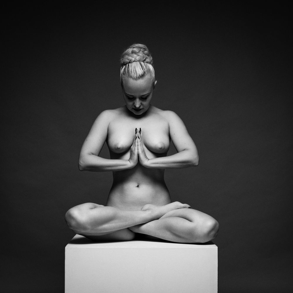 An art nude model poses for a black and white fine art nude image in a studio

She is sat on a posing block in the lotus yoga position
