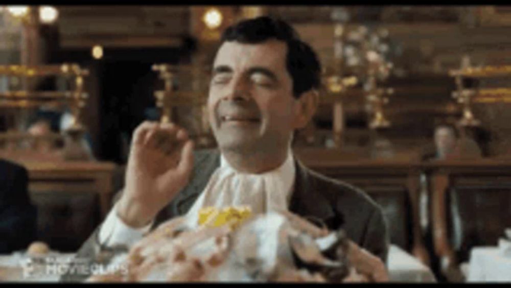 a man in a suit and tie is sitting at a table with a plate of food on it .