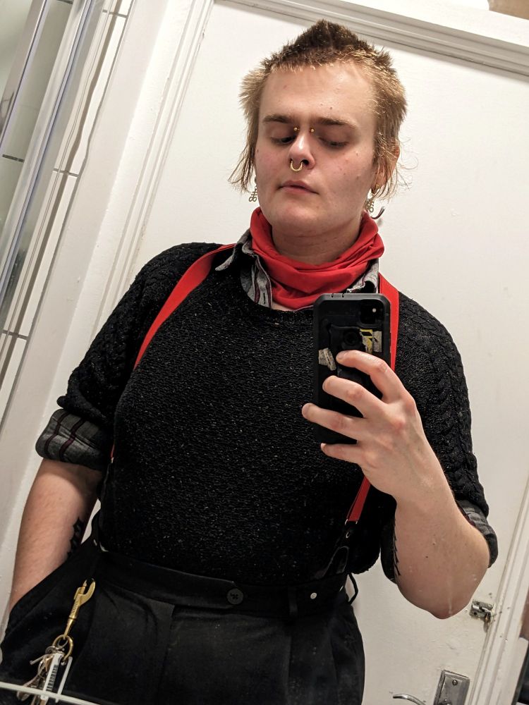 butch trans woman, grade 6ish hair, red neck scarf, red braces. gold face jewelry, jumper/flannel combo. cxnty hips.