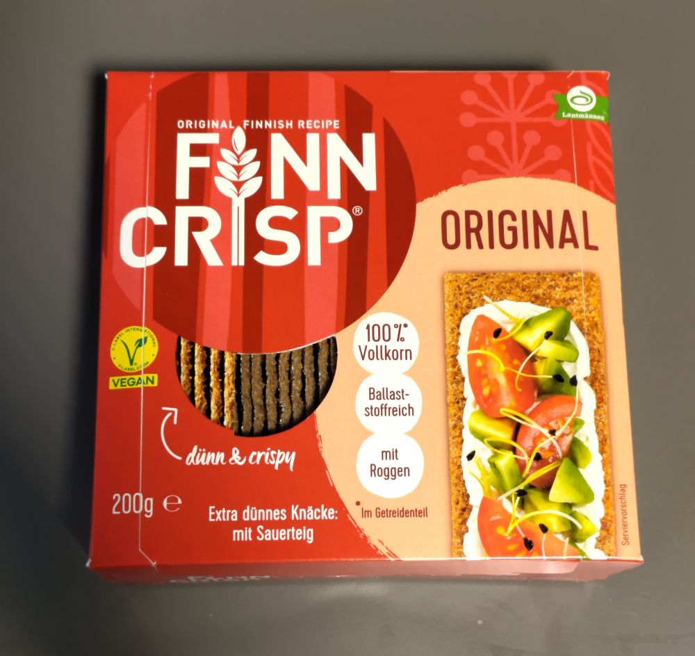 Das Bild zeigt eine rote Verpackung des Produkts Finn Crisp Original, einem finnischen Knäckebrot.

Hier sind die Details der Verpackung:

Oben steht: "Original Finnish Recipe" (Original finnisches Rezept).

In der Mitte ist das Markenlogo FINN CRISP mit einer stilisierten Ähre zwischen den Worten.

Darunter steht: "dünn & crispy".

Auf der rechten Seite ist ein Bild einer Scheibe Knäckebrot mit Belag aus Avocado, Tomaten und Sprossen.

Es wird hervorgehoben, dass das Produkt 100 % Vollkorn, Ballaststoffreich und mit Roggen ist.

Unten links steht das Gewicht: 200 g.

Außerdem ist ein vegan-Label zu sehen (grünes Symbol mit dem Wort „VEGAN“).

Weitere Texte: „Extra dünnes Knäcke: mit Sauerteig“ und „Im Getreideanteil“.


Die Verpackung hat ein modernes, klares Design in Rot- und Beigetönen, typisch für gesunde Vollkornprodukte.