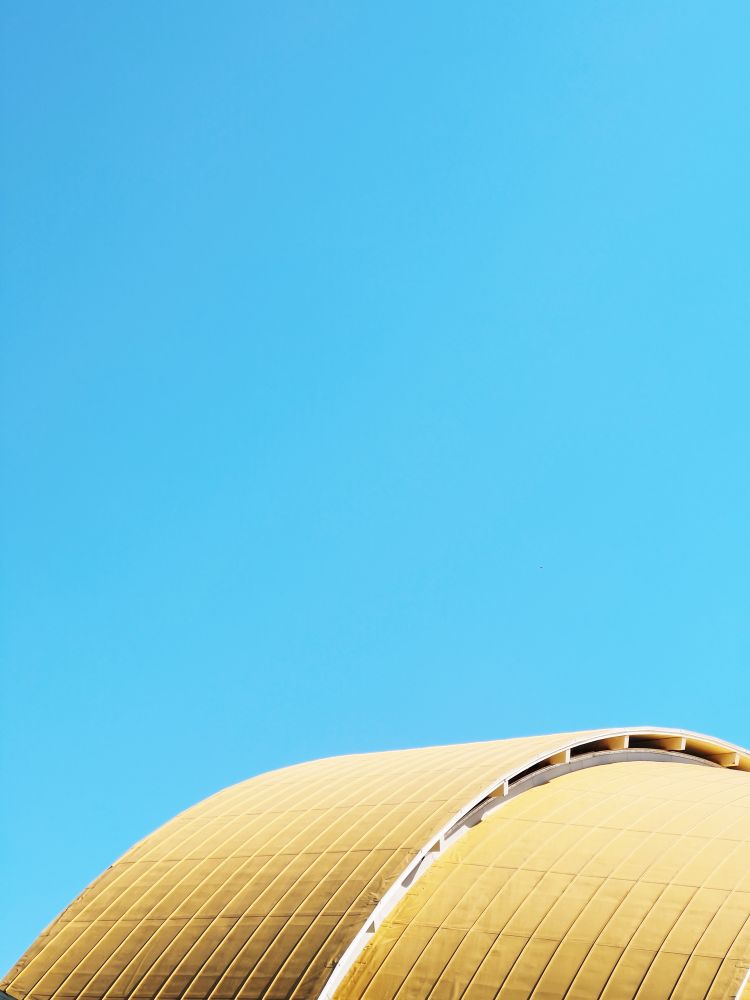 A crisp, clear blue sky. At the bottom of the frame, the top of a golden dome that arches across the lower third. It gleams from sunlight originating from behind. 