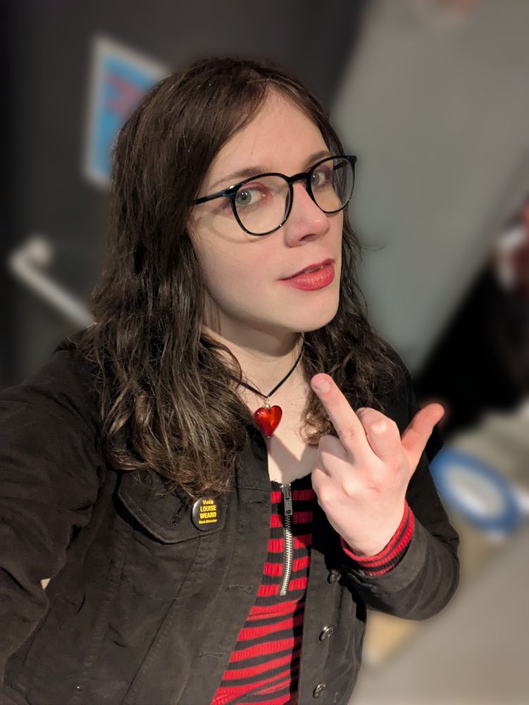 Kit in an accessible bathroom throwing up a middle finger with the thumb sticking out in a red and black striped top with zip, red heart pendant necklace and black denim jacket with red eyeshadow and lipstick 


She's at least a little glassy eyed
