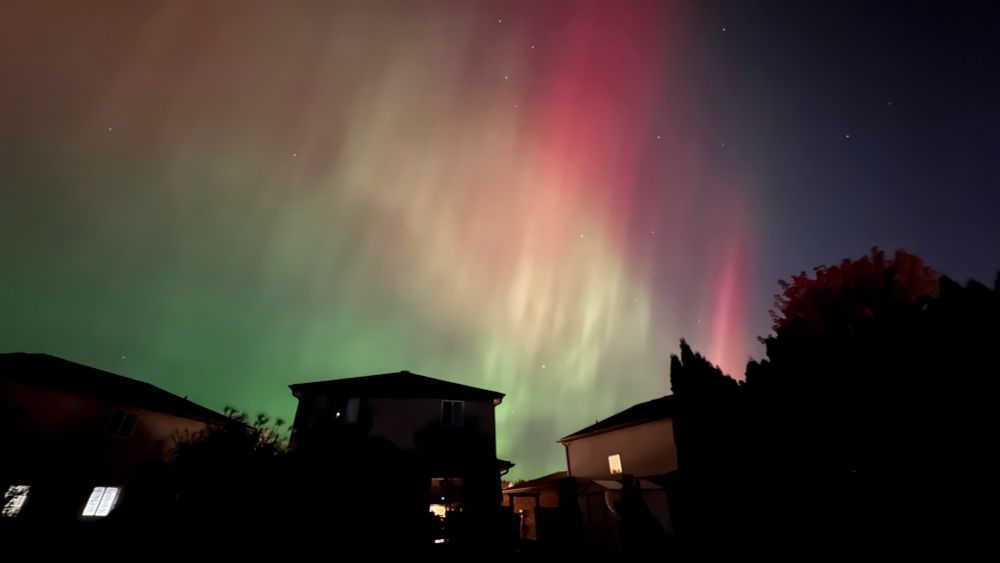 Colors such as red, green, yellow are spread across the sky in the top half of the image. In the bottom half are the homes in silhouette highlighted from the Auroral displays!